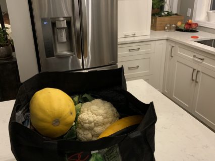 Fresh vegetables sitting on a kitchen counter in a reusable bag.