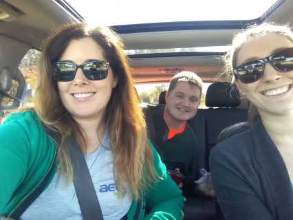 Two women and a man carpooling together and leaning in to smile for a picture.