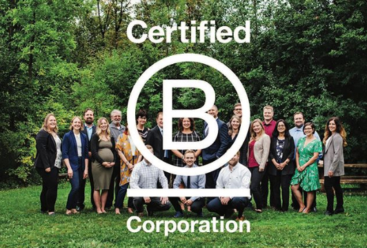 bcorp AET Group employees standing in a group and smiling towards camera. The Certified B Corporation logo is overlaid on image.