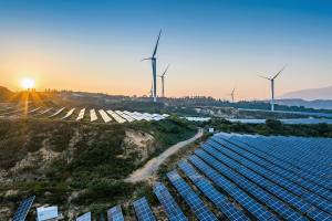 A picture of a solar panel farm at sunset with windmills in the background.