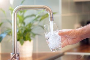 A person holding a glass being filled up with tap water.