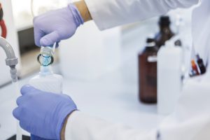 iStock-852586170-resized A person wearing nitrile gloves pouring water from a test tube into a container.